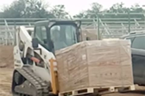 Bobcat Skid-Steer with fork life attachment carrying solar panels.