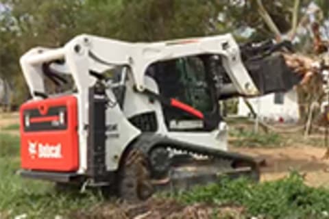 Bobcat S770 Skid-Steer Loader with root grapple attachment carrying trees